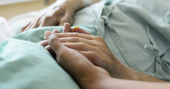 A young hand touches and holds an old wrinkled hand in hospital