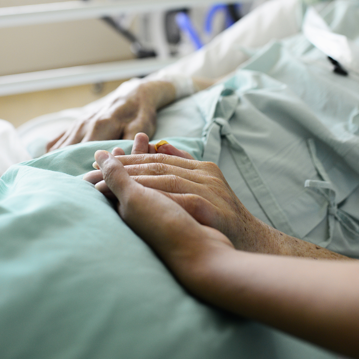 A nurse and patient touch hands in a hospital.
