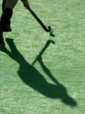 The shadow of a field hockey player as they run down the pitch.