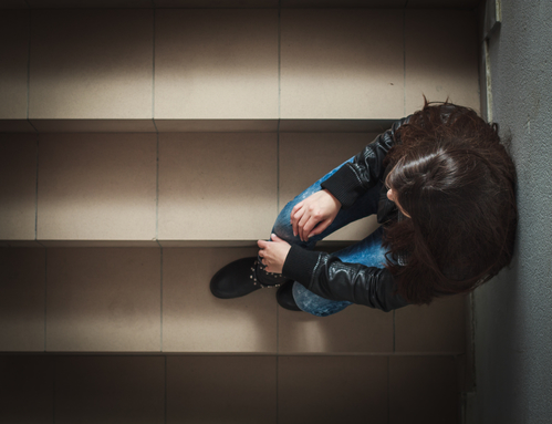 Depressed teenage girl with hands over face sitting on the stairs.
