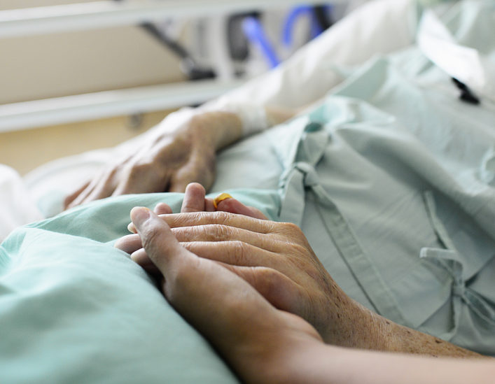 A nurse and patient touch hands in a hospital.