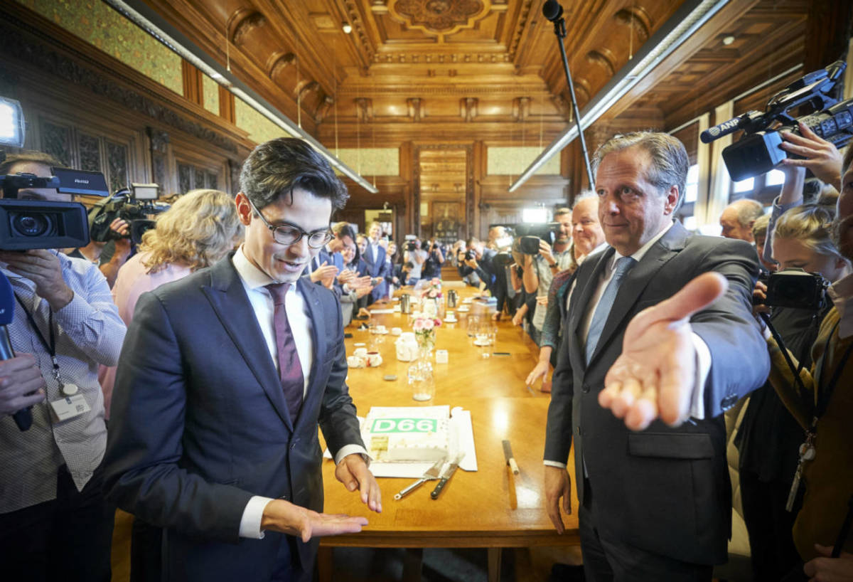 New D66 leader Rob Jetten standing next to his predecessor Alexander Pechtold, who is gesturing towards the exit of the party's conference room at the Binnenhof in The Hague.