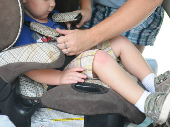 A woman strapping a young child into a car seat.