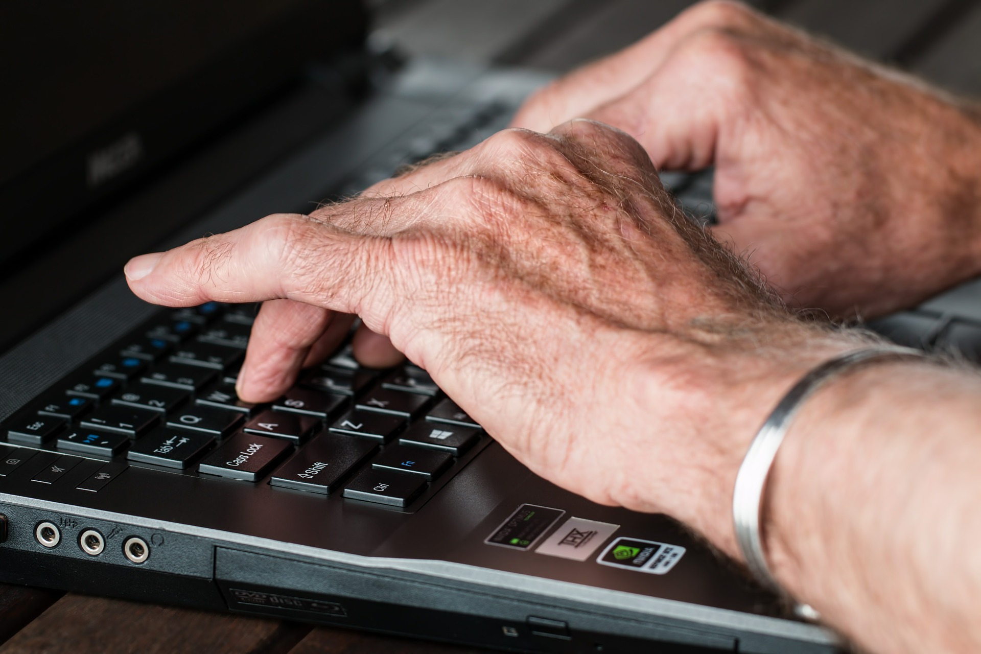 old person hands typing at a laptop in close-up