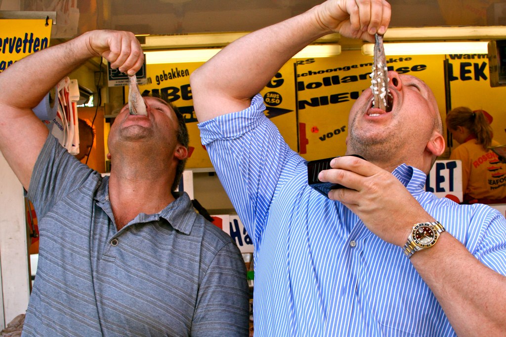 Two men eating new herring in the traditional way, by dropping it into their mouths