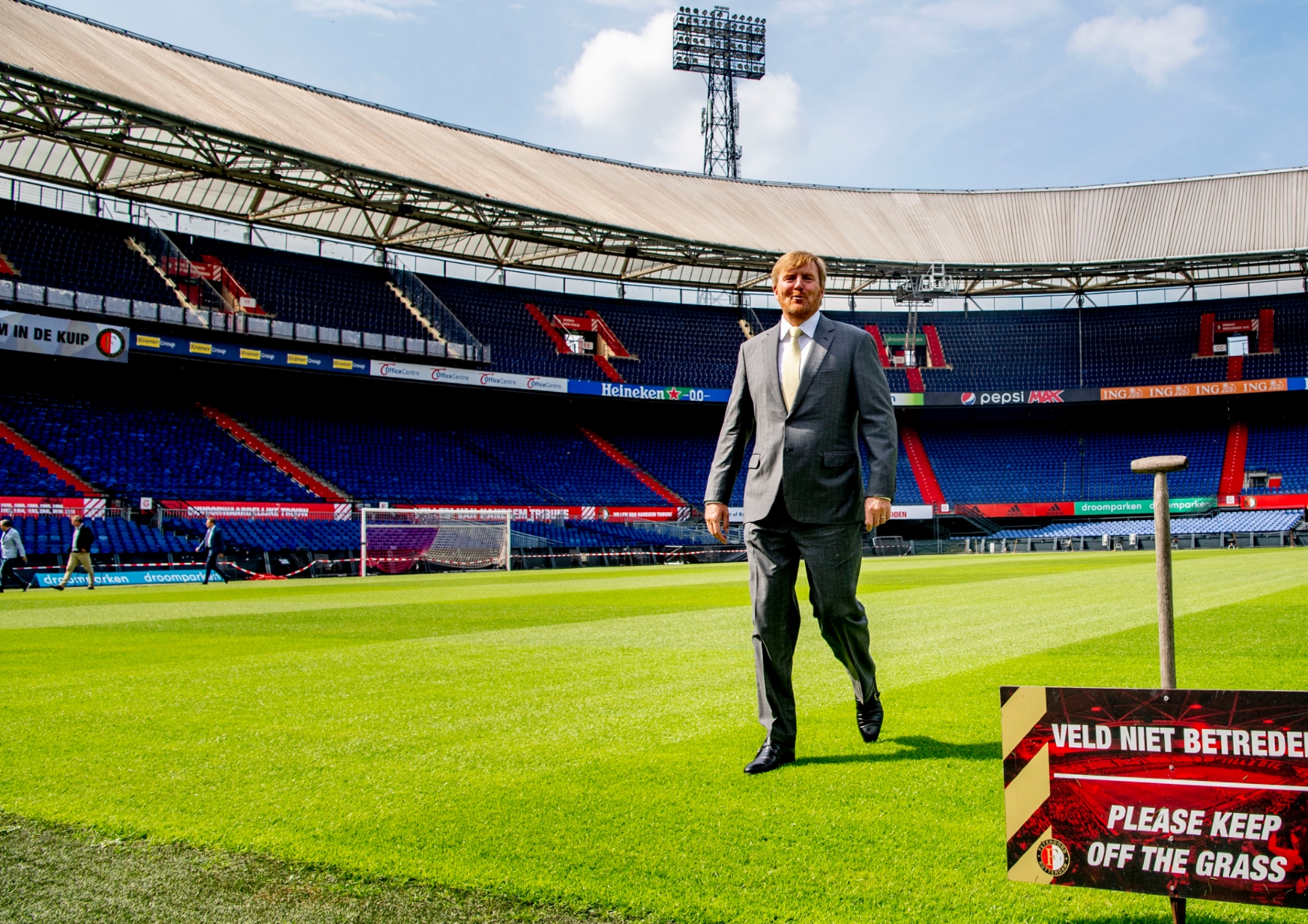 King Willem-Alexander walking on the pitch at Feyenoord past a sign saying 'keep off the grass'
