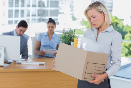 A woman carrying a box of items away from her desk in an office