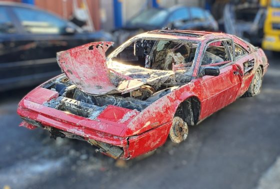 The rusted shell of the red Ferrari Mondial viewed from front.