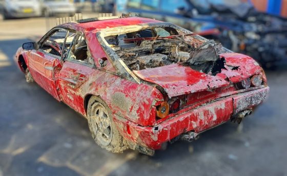 The rusted shell of the red Ferrari Mondial viewed from behind.