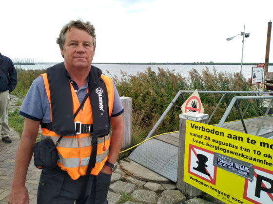 Arie Kappert in an orange life vest beside a sign at the staithe in Almere where recovered pieces of plane are landed.