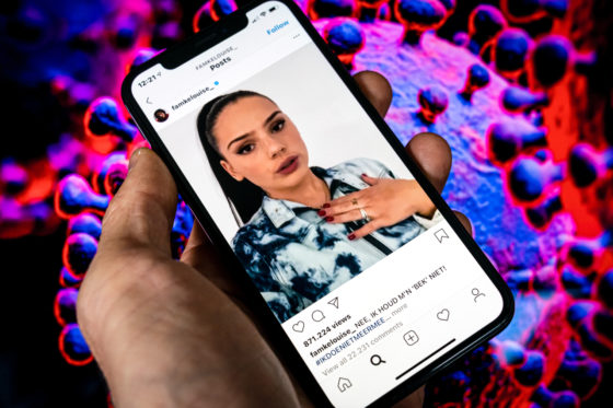 A phone showing Famke Louise's Instagram account in front of a visual representation of coronavirus